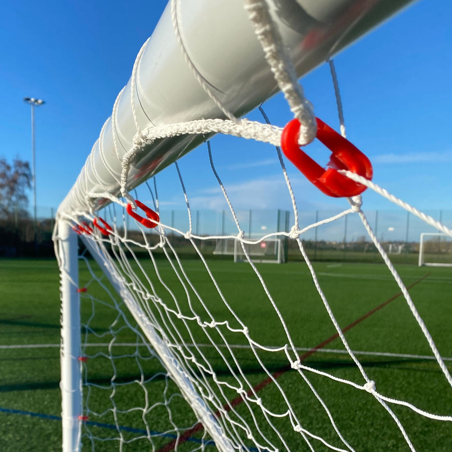 Red Q-FOLD net clips holding a white net to a white goal crossbar, close up on an artificial field.