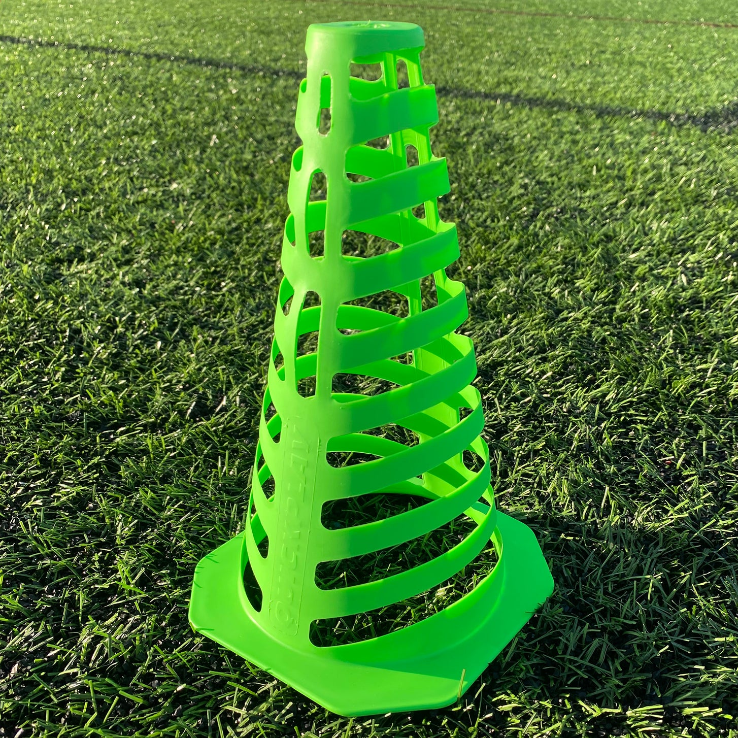 One green 9" Tall Collapsible Cone close up on artificial turf, showing its slotted sides and flat base.