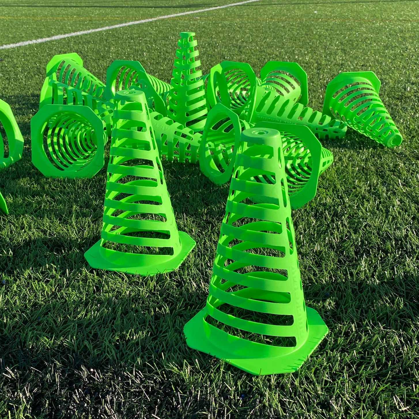 Bright green 9" Tall Collapsible Cones in a pile, some standing and some on their sides, on artificial turf in the sun.