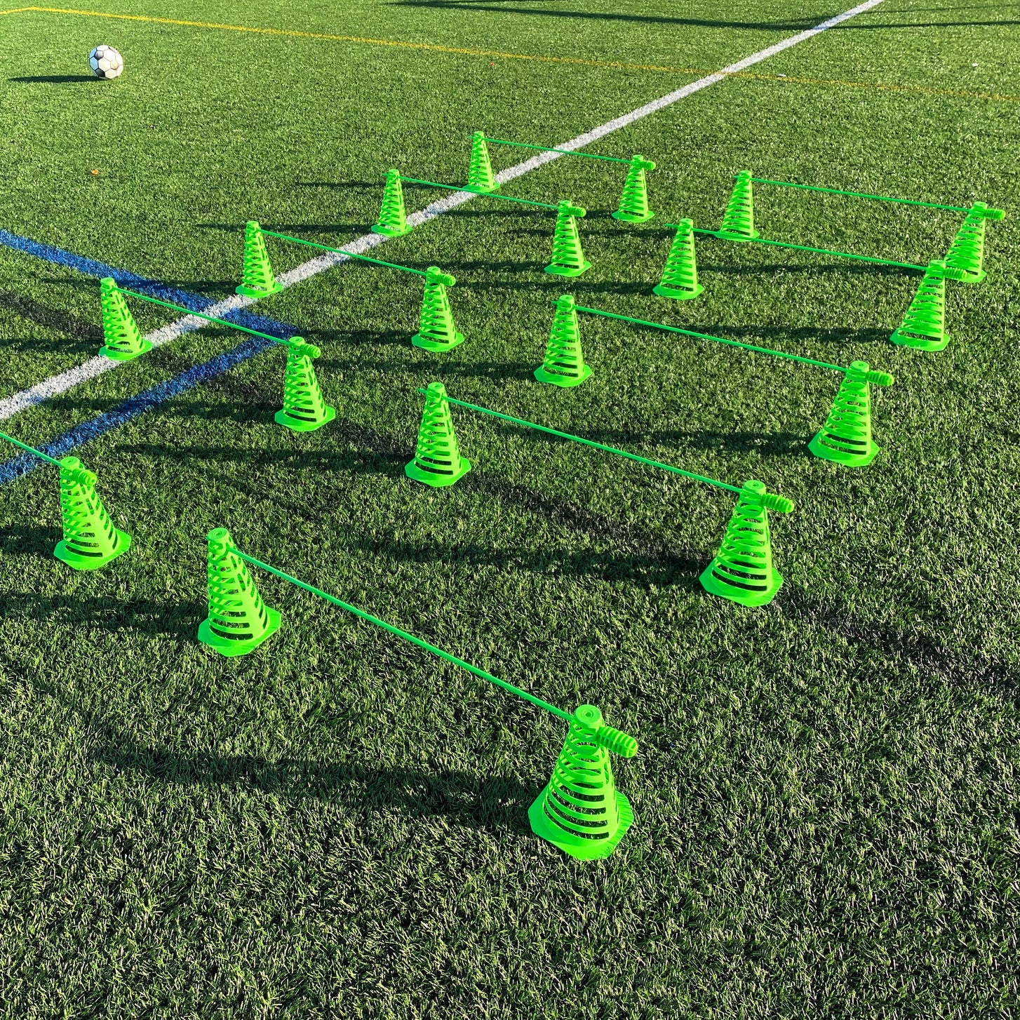 Rows of green 9" Tall Collapsible Cones joined by green poles as hurdles on an artificial field, with a soccer ball behind.