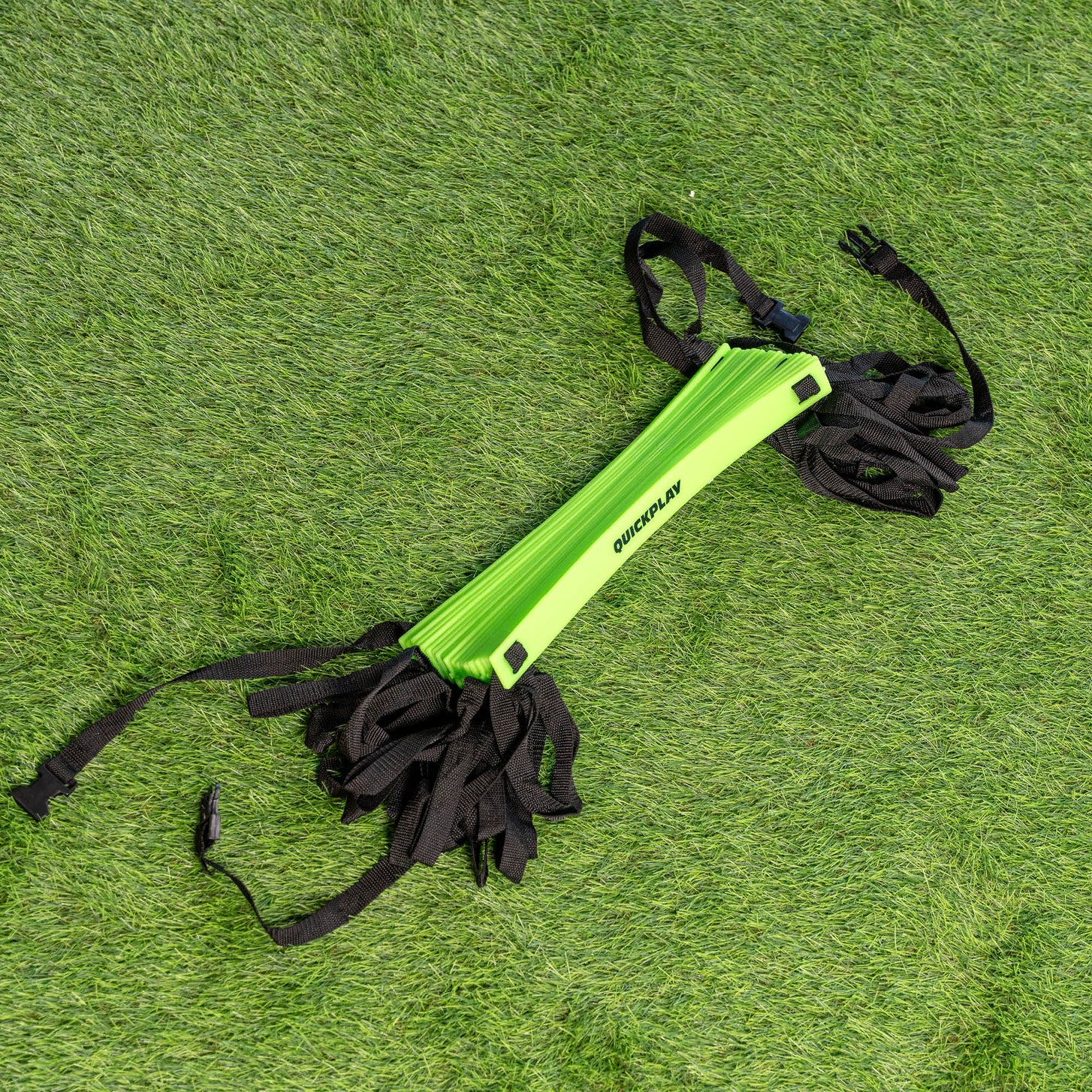 Agility Ladder XXL 30ft folded up with the green rungs stacked together and the black straps bundled at each end, on artificial grass.