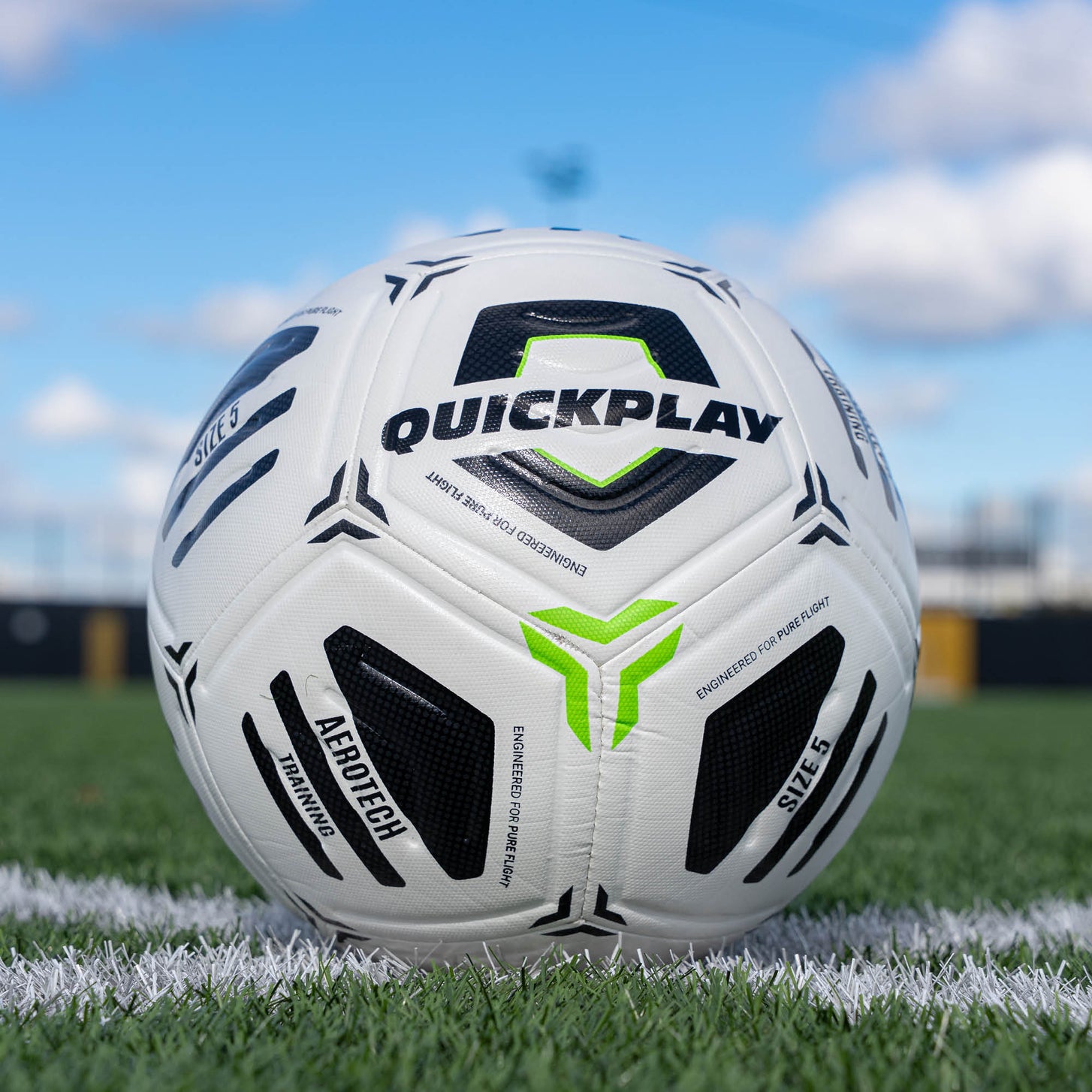 White Aerotech soccer ball with black and green accents on a grass field, featuring the Quickplay brand.