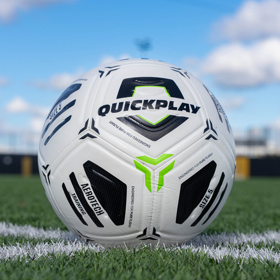 White Aerotech soccer ball with black and green accents on a grass field, featuring the Quickplay brand.