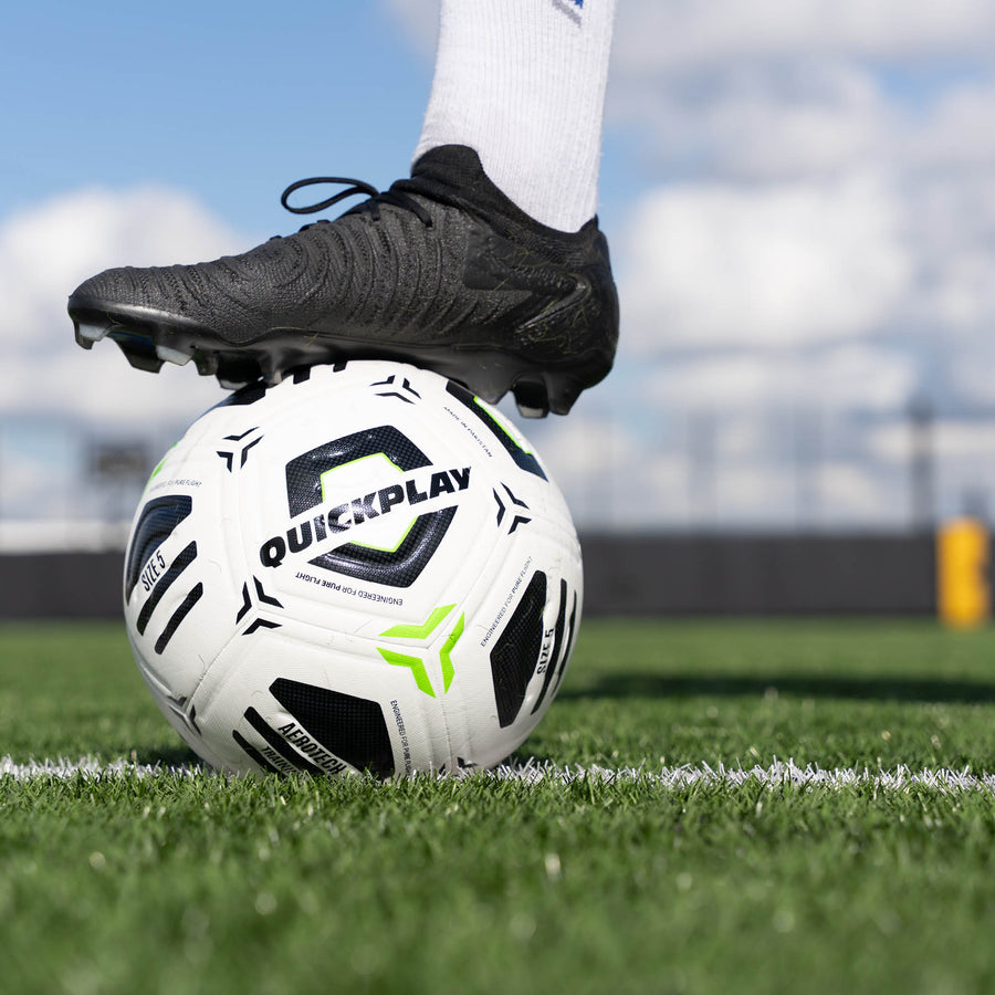 Aerotech Soccer ball with 'QuickPlay' branding on a grass field, foot wearing a black cleat on top.