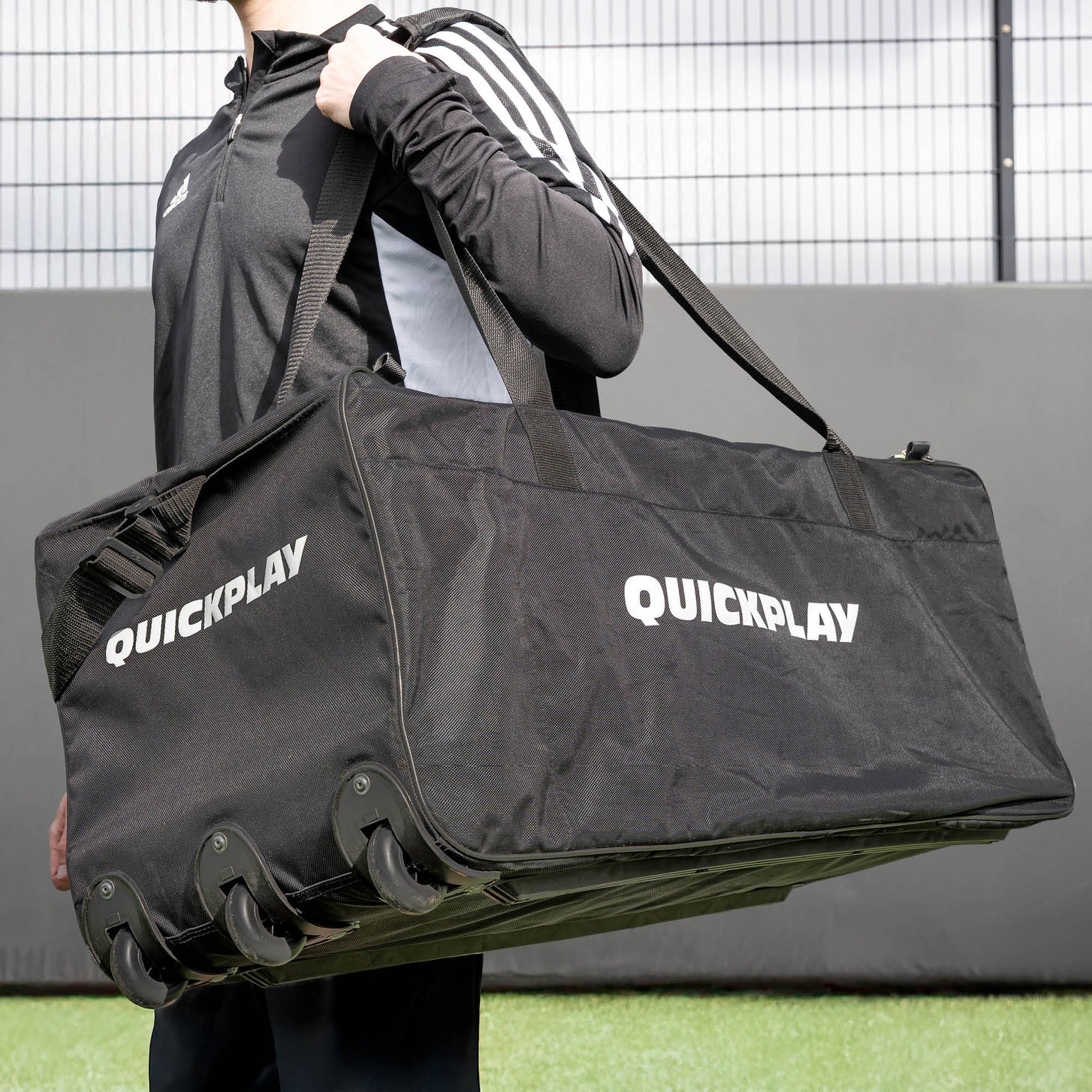 Man carrying the Equipment Bag with Wheels (XL) on his shoulder by its strap, with the wheels visible along the base.