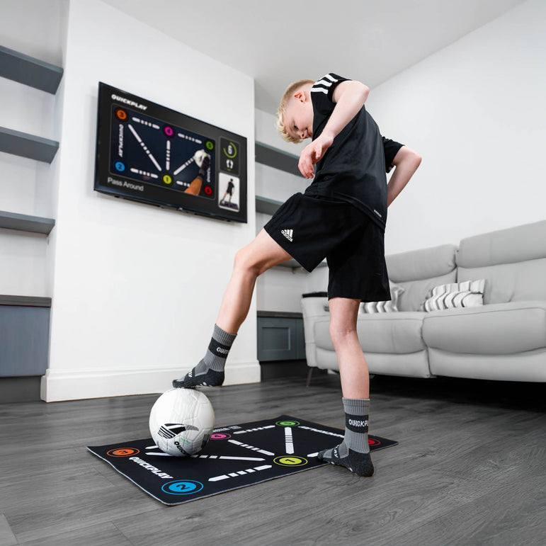Child playing with a soccer ball on an ball mastery skills mat in a living room.