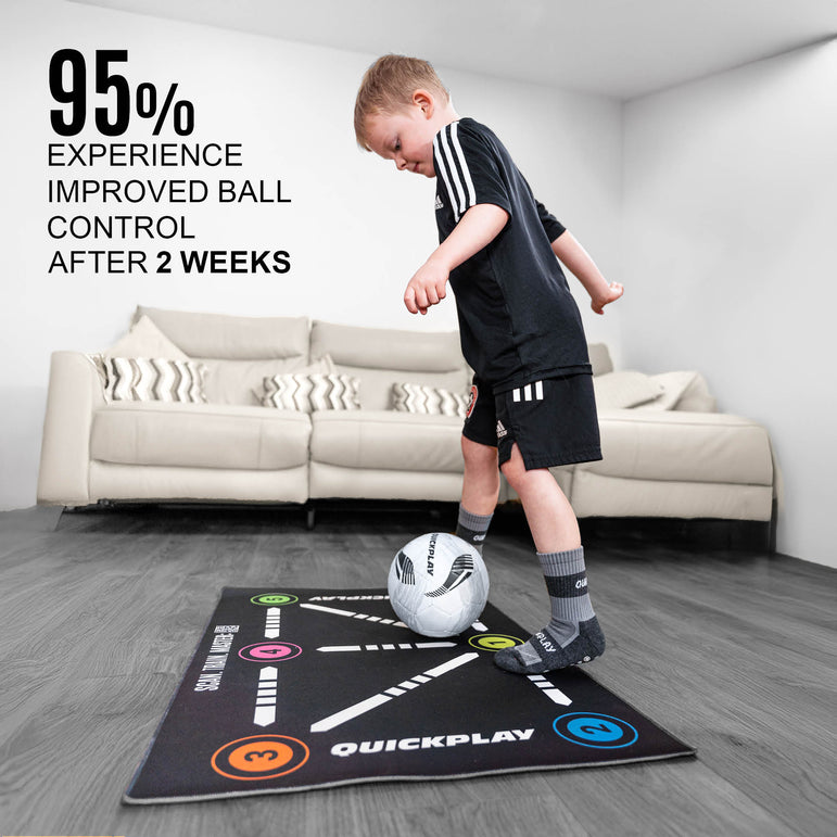 Child playing with a soccer ball on a QUICKPLAY ball mastery mat in a living room.
