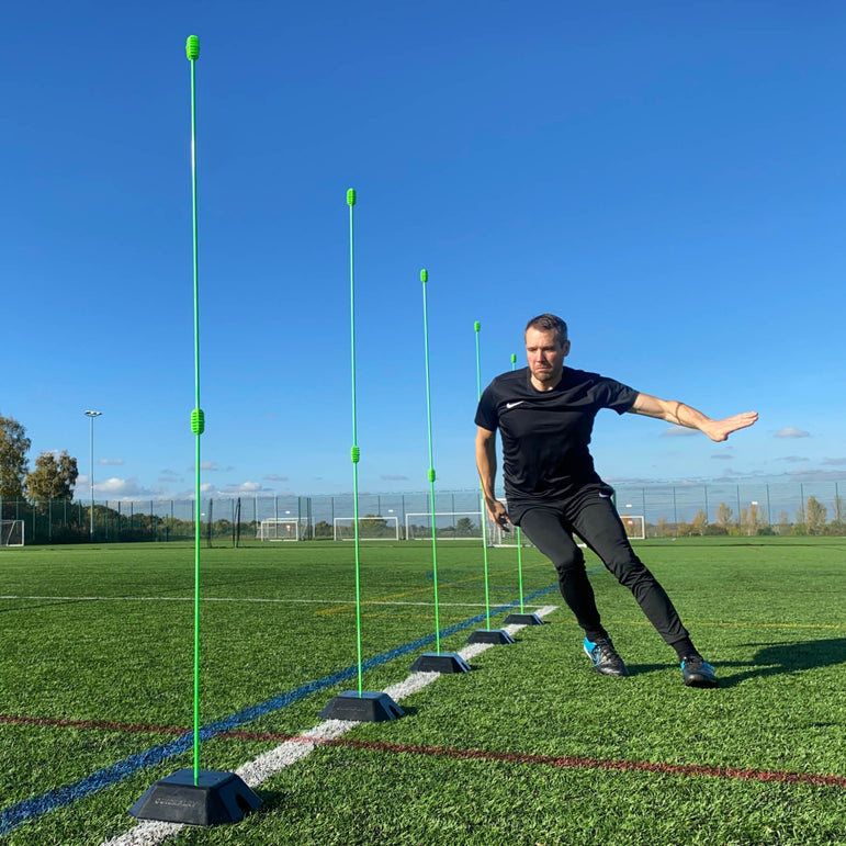 Person practicing agility drills with QUICKPLAY green agility poles on a sports field