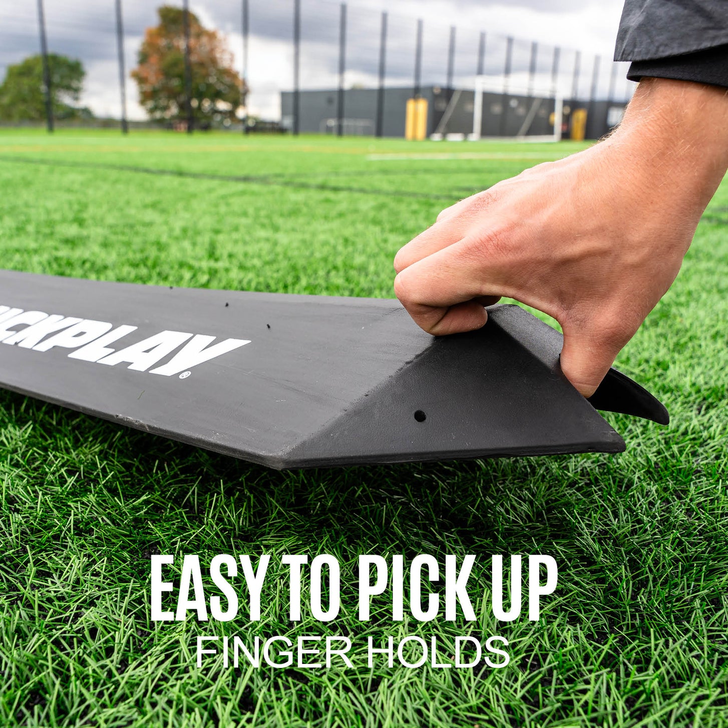 Hand lifting the end of the Goalkeeper Deflection Ramp by its finger hold on turf, with the text "Easy to pick up, finger holds".