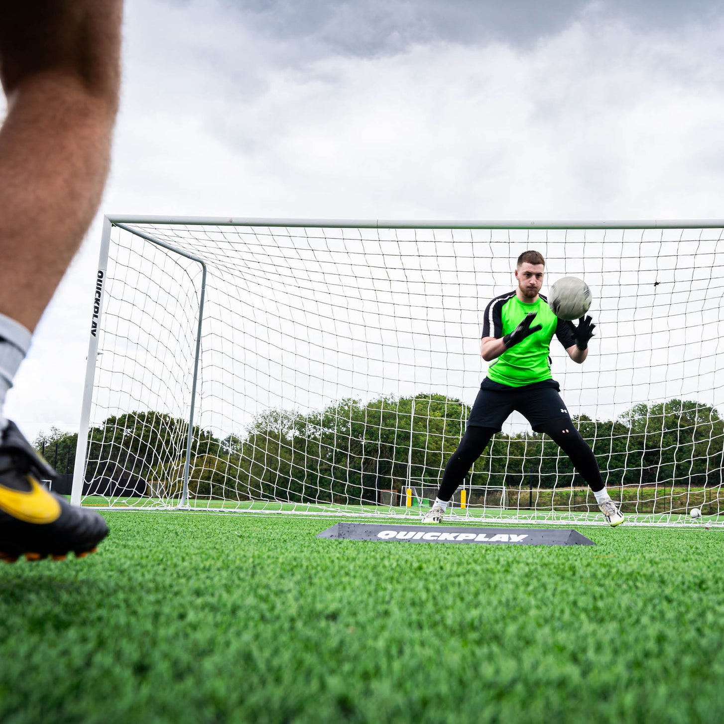 Goalkeeper Deflection Ramp in front of a goalkeeper catching a ball at chest height, seen from beside the shooter's foot.