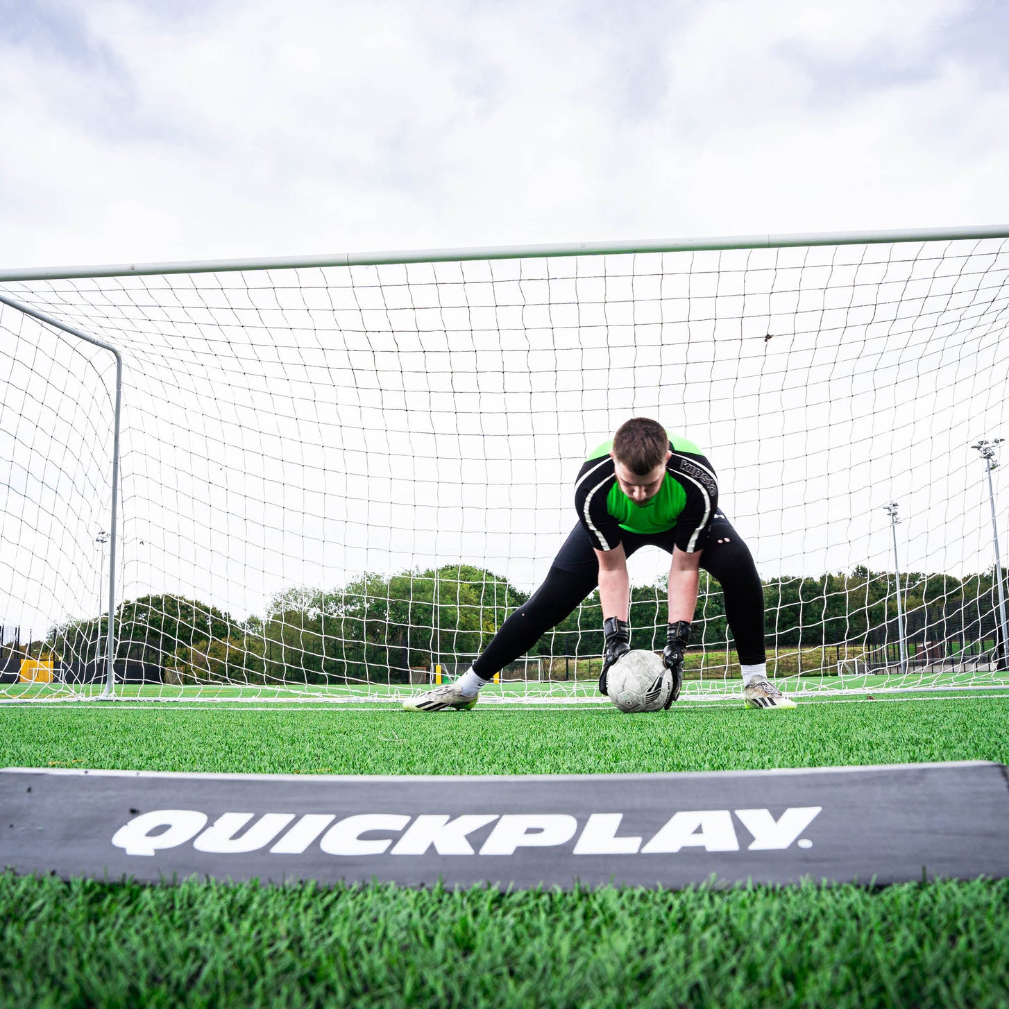 Goalkeeper crouching to gather a low ball in goal, seen from behind the Goalkeeper Deflection Ramp in the foreground.
