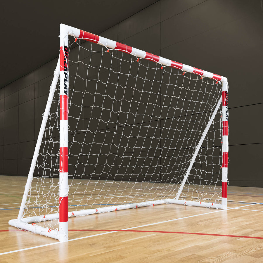 QUICKPLAY Handball goal with red and white frame on a wooden floor against a dark wall.