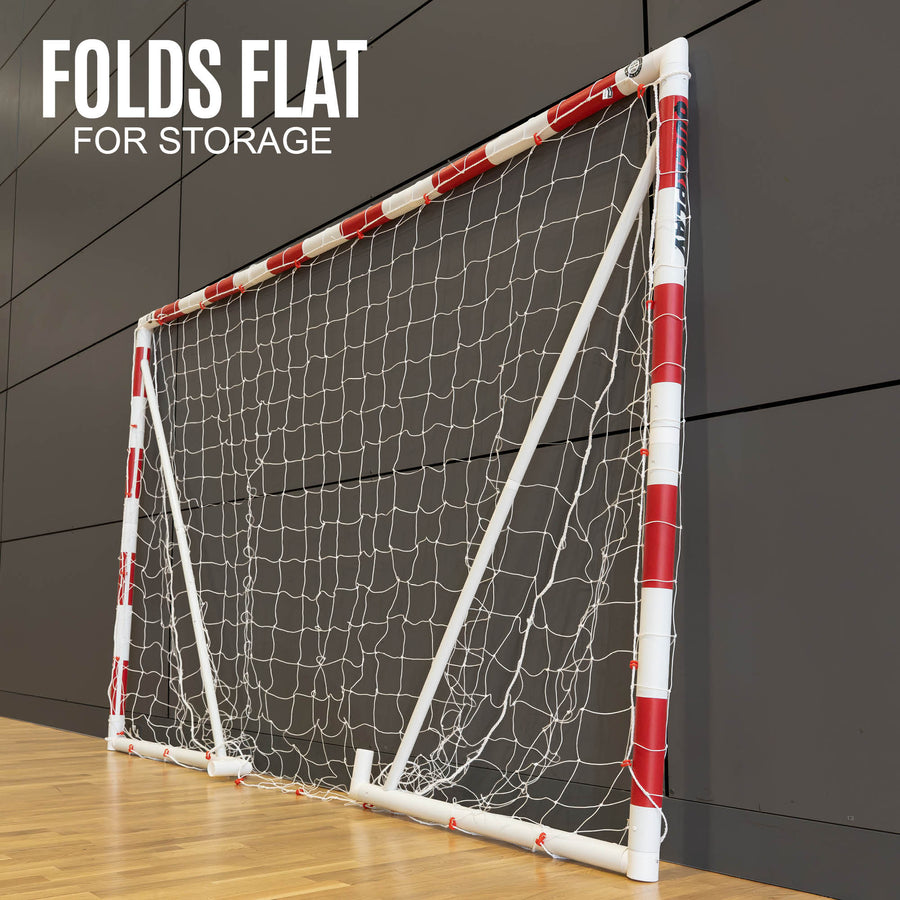 Portable Handball goal with red and white design folded on a wooden floor against a dark paneled wall.