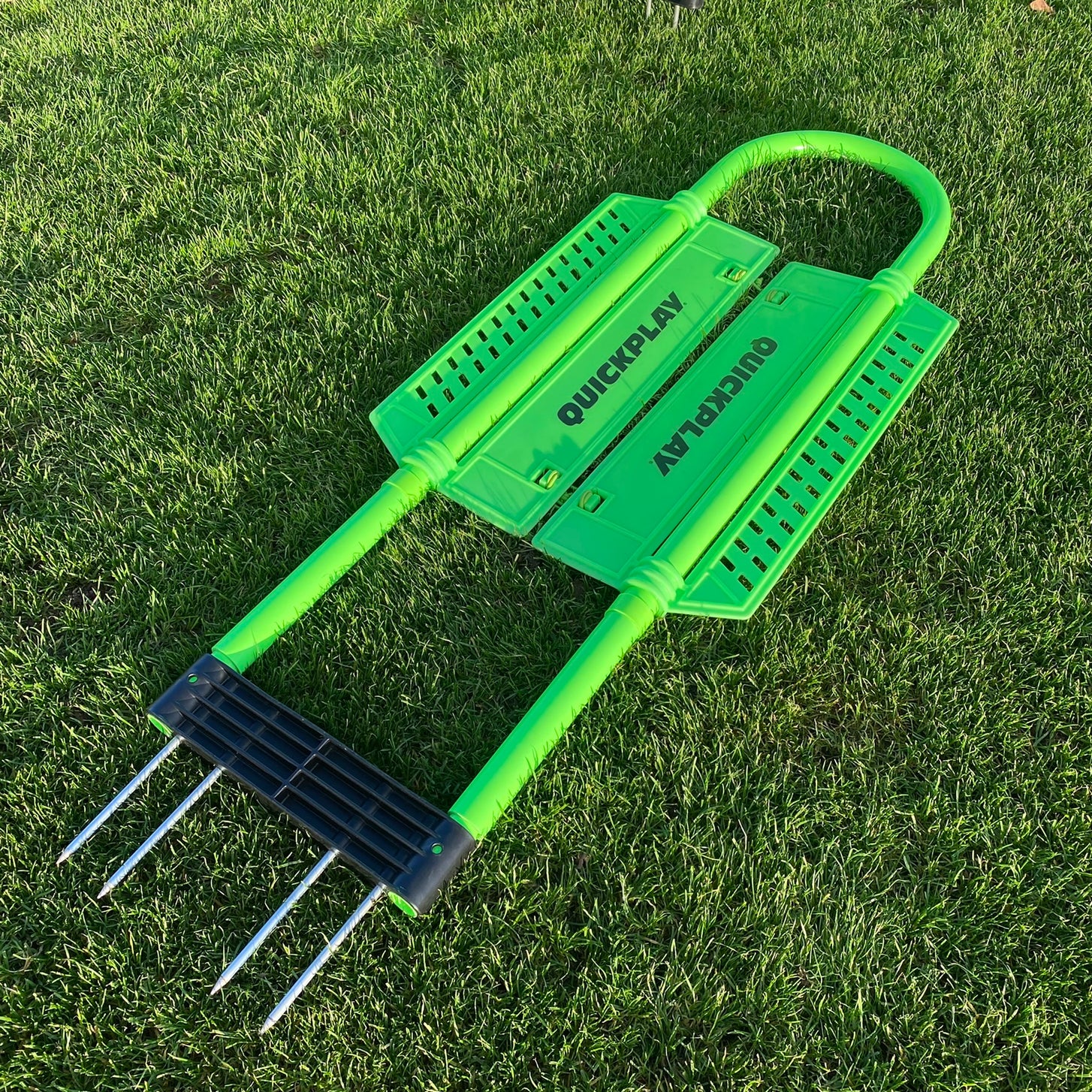 REPLAY Defender Mannequin lying flat on grass, showing its green frame, side panels and the four metal spikes under the black base.
