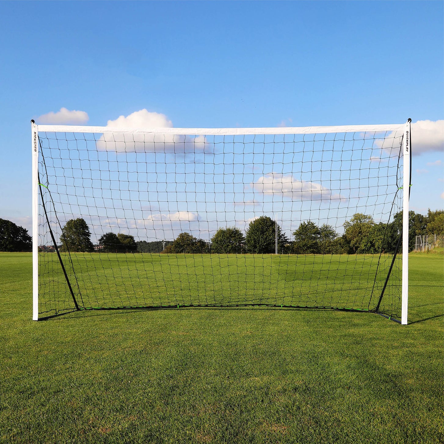 KICKSTER 12x6' goal from straight in front on a grass field, white frame and black net against a blue sky.