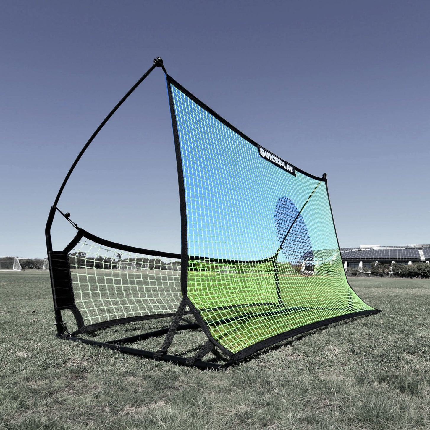 Green and blue TEKKERS Trainer net with a blue target circle, fitted on its black frame on a grass field.