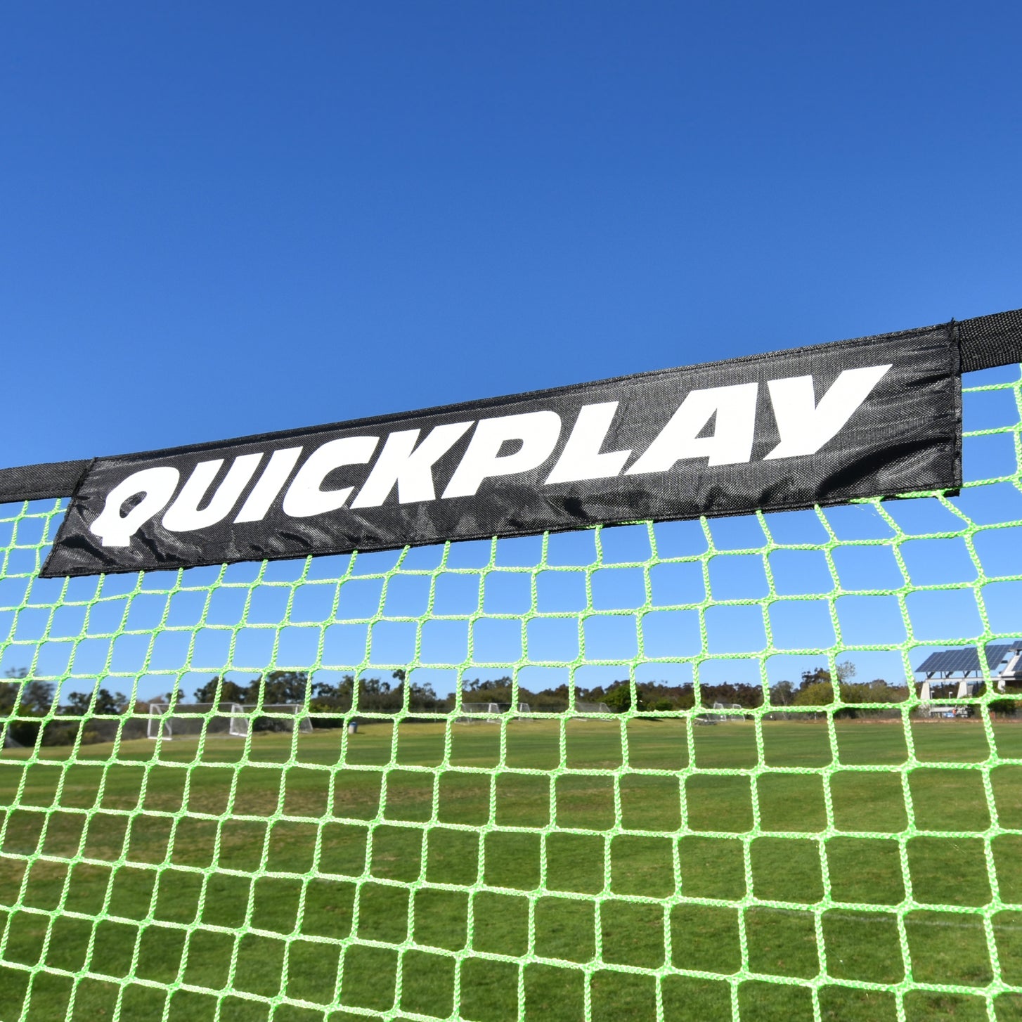 Close-up of the green TEKKERS Trainer net with a black QUICKPLAY banner along the top, against a blue sky.