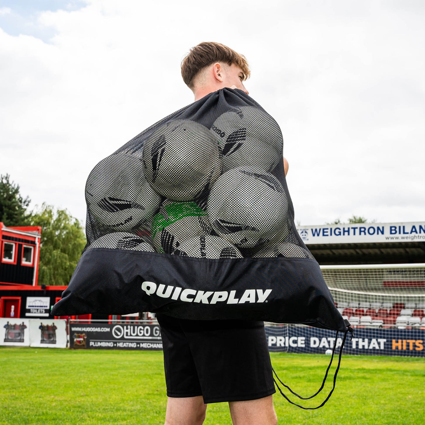 Player carrying the Mesh Soccer Ball Bag full of soccer balls over his shoulder at a soccer stadium.