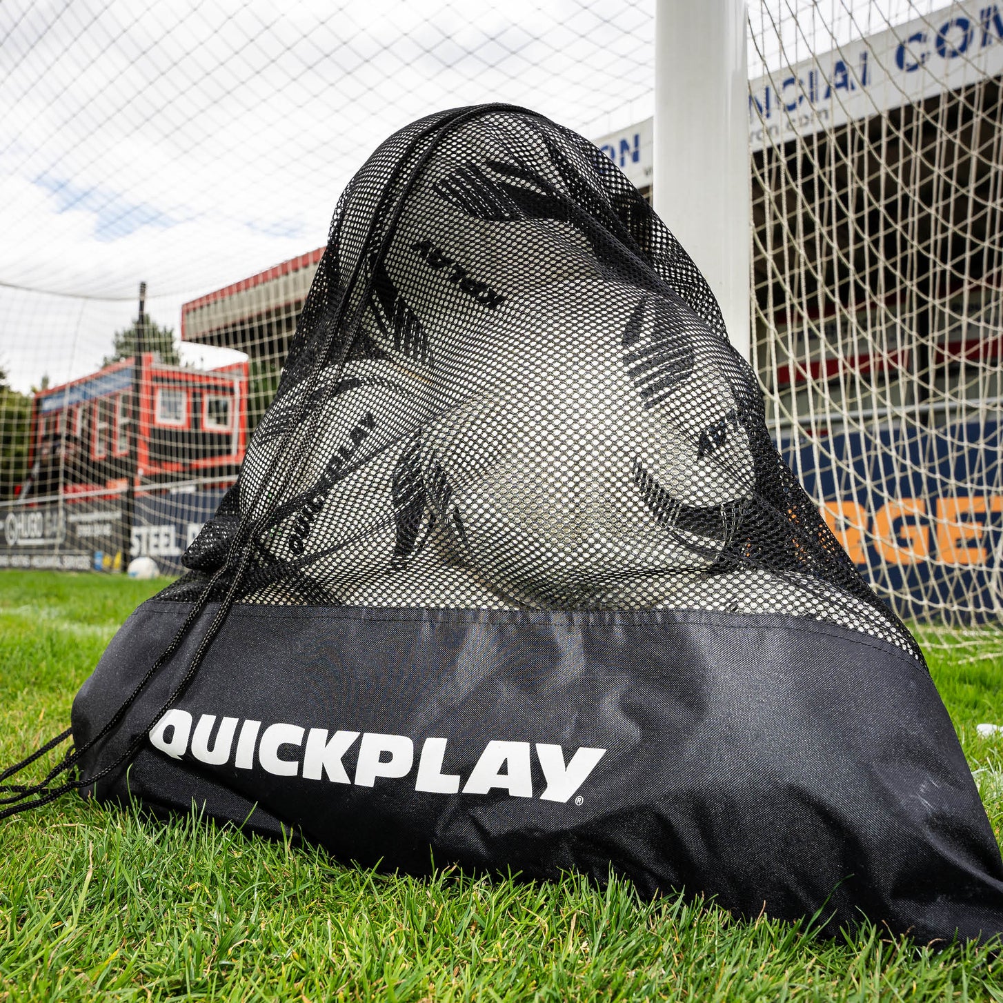 Mesh Soccer Ball Bag full of soccer balls sitting on grass in front of a goal net.