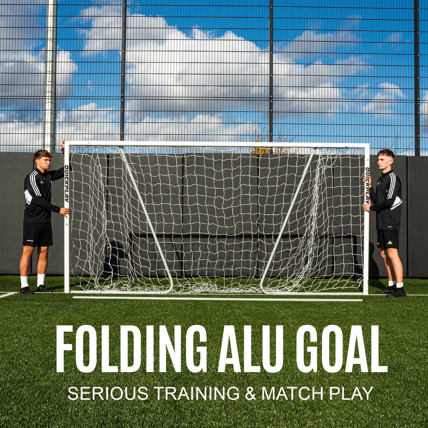 Two players holding the PRO ALU Match60 Futsal Goal 9.8x6.5' upright against a fence, with the text "Folding ALU goal".