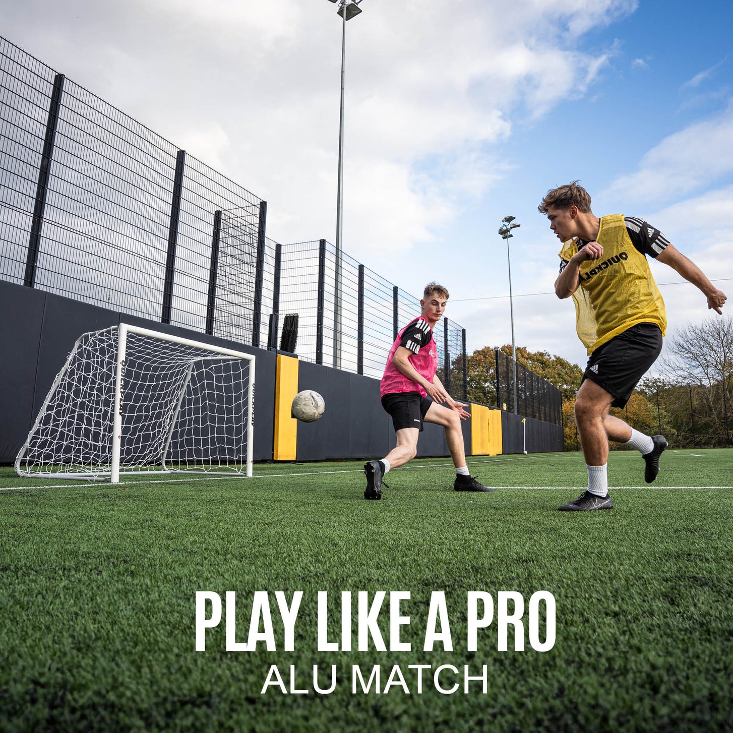 PRO ALU Match60 8x5' goal by a wall on artificial turf as two players in bibs compete for a soccer ball, with the text "Play like a pro, ALU Match".