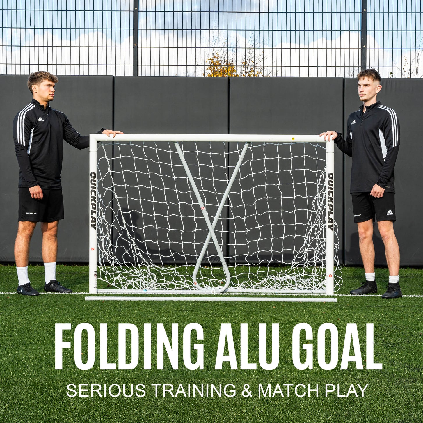 PRO ALU Match60 8x5' goal held upright by two players on artificial turf in front of a fence, with the text "Folding ALU goal, serious training & match play".