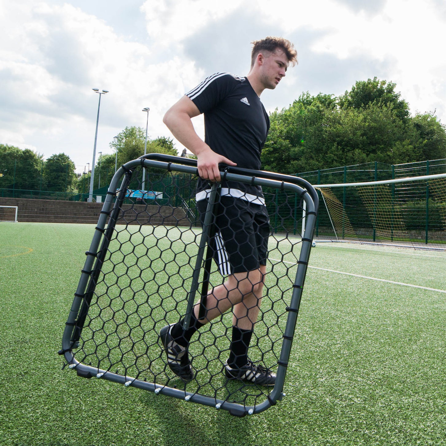 Player carrying the PRO Rebounder 3x3' by its frame across an artificial field.