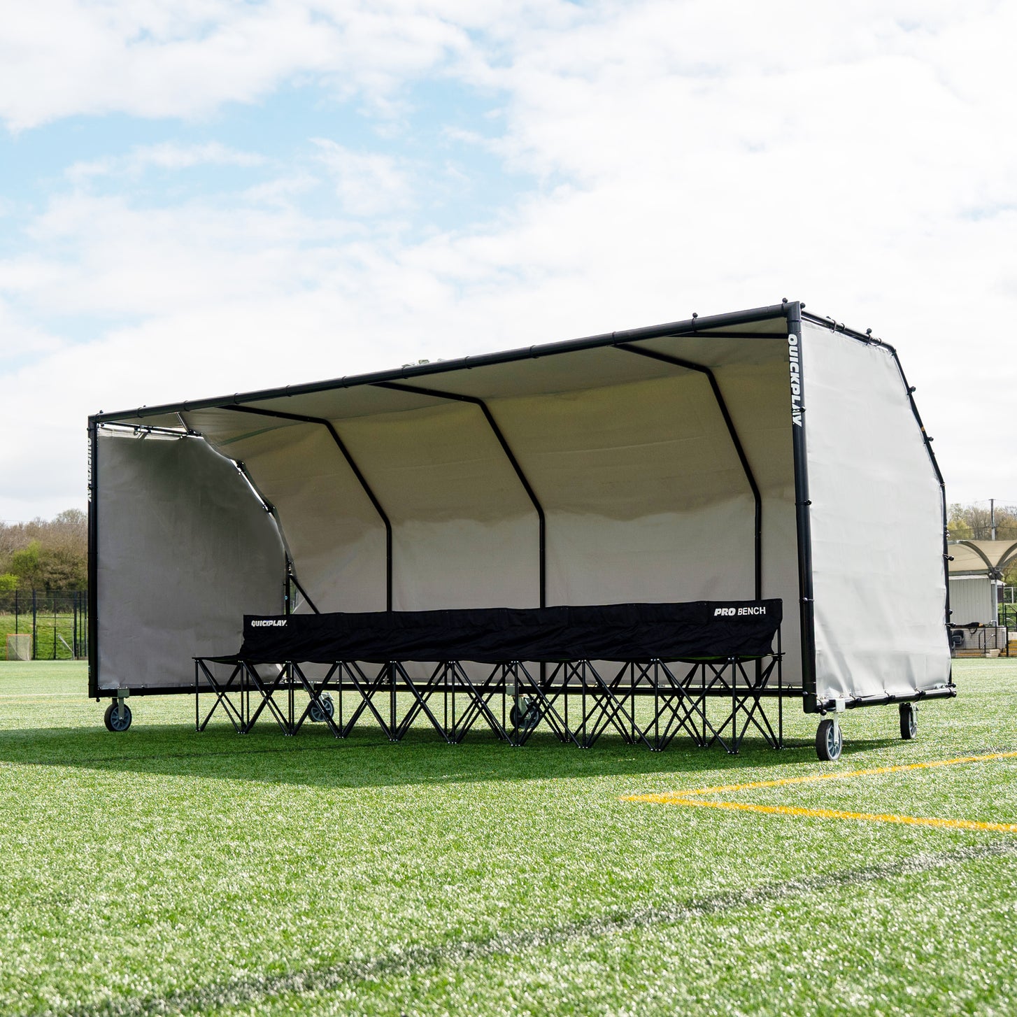 PRO ALU Club Shelter 16x6' on an artificial field, seen at an angle, with a black bench marked PRO BENCH inside.