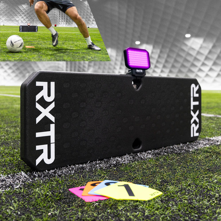 Black RXTR training board on a soccer field with a player and soccer ball in the background.