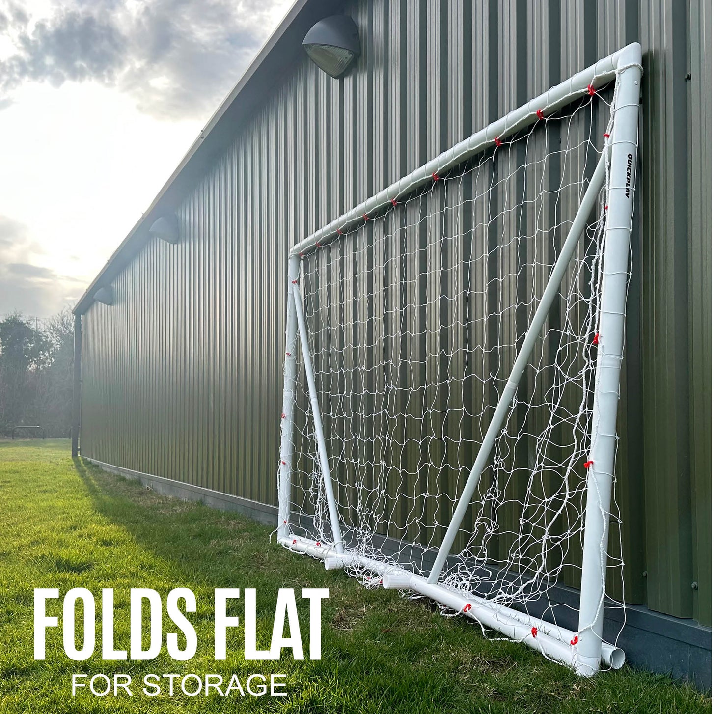 Q-FOLD 10x6' goal folded flat against a green metal building wall, with the text "Folds flat for storage".