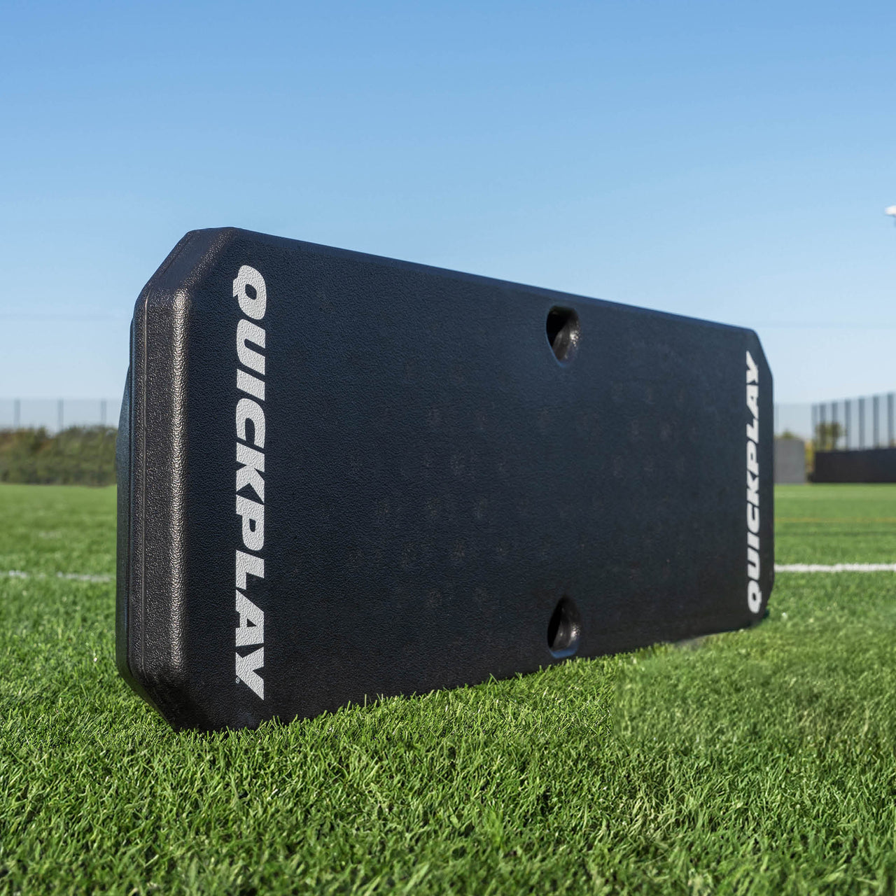 Black QuickPlay REPLAY BOOMBOX  rebound board on a grass field with a clear blue sky.