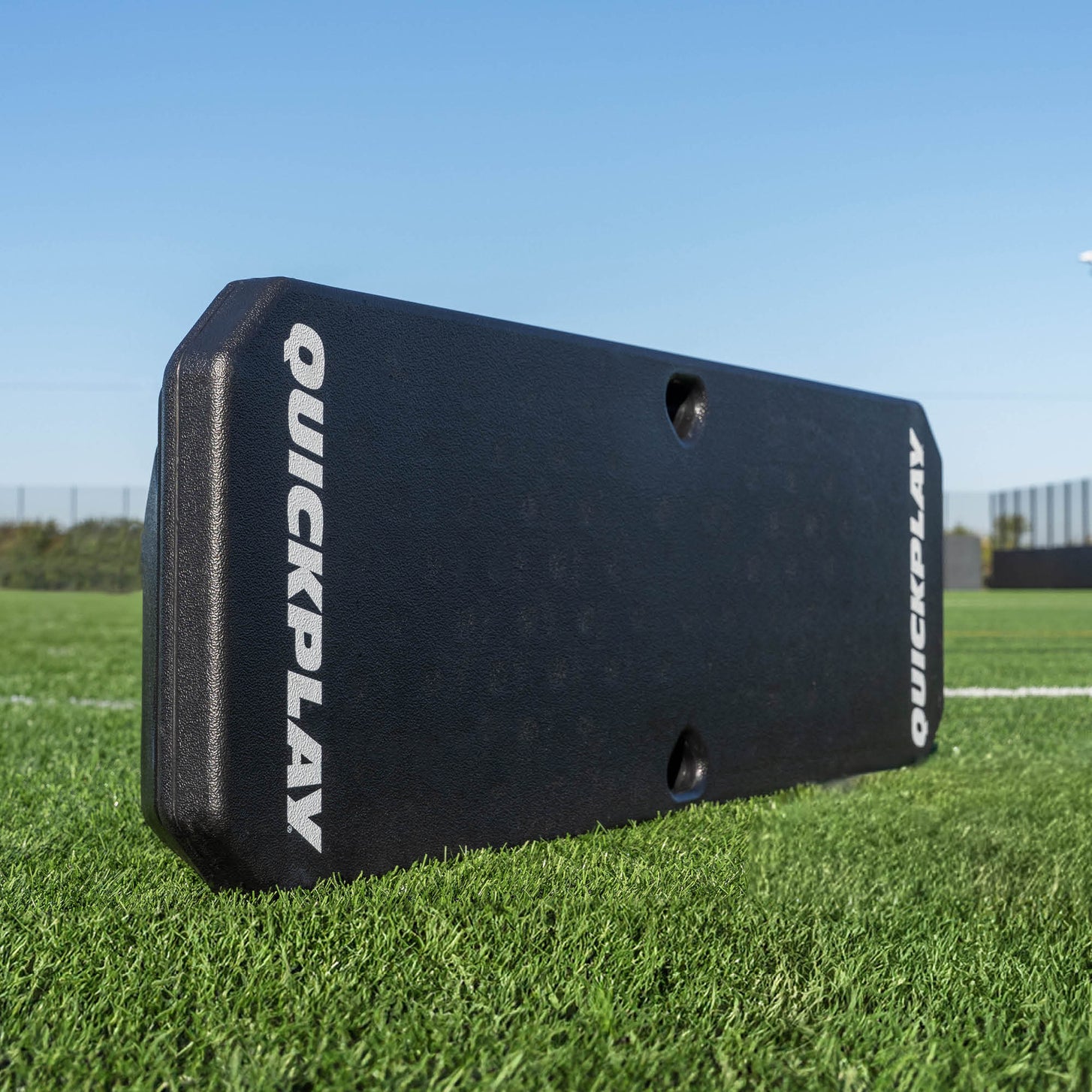 Black QuickPlay REPLAY BOOMBOX  rebound board on a grass field with a clear blue sky.
