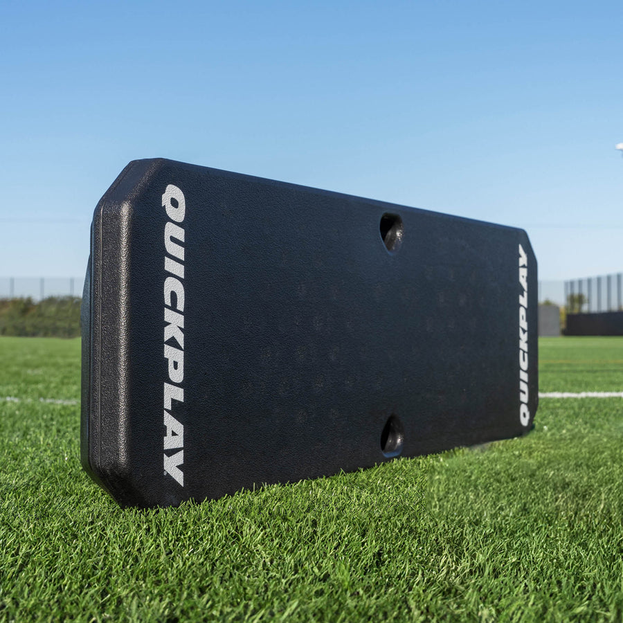 Black QuickPlay REPLAY BOOMBOX  rebound board on a grass field with a clear blue sky.