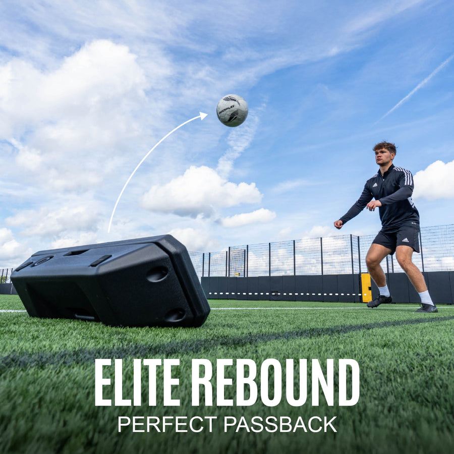 Person practicing soccer passbacks with a rebounder on a sports field.