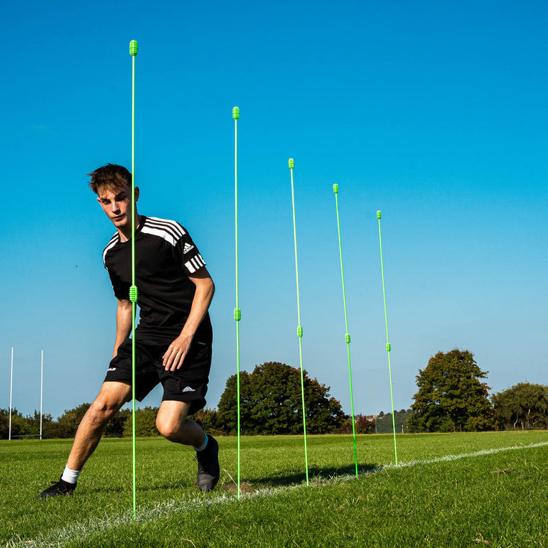 Person on a soccer field with green training markers against a blue sky