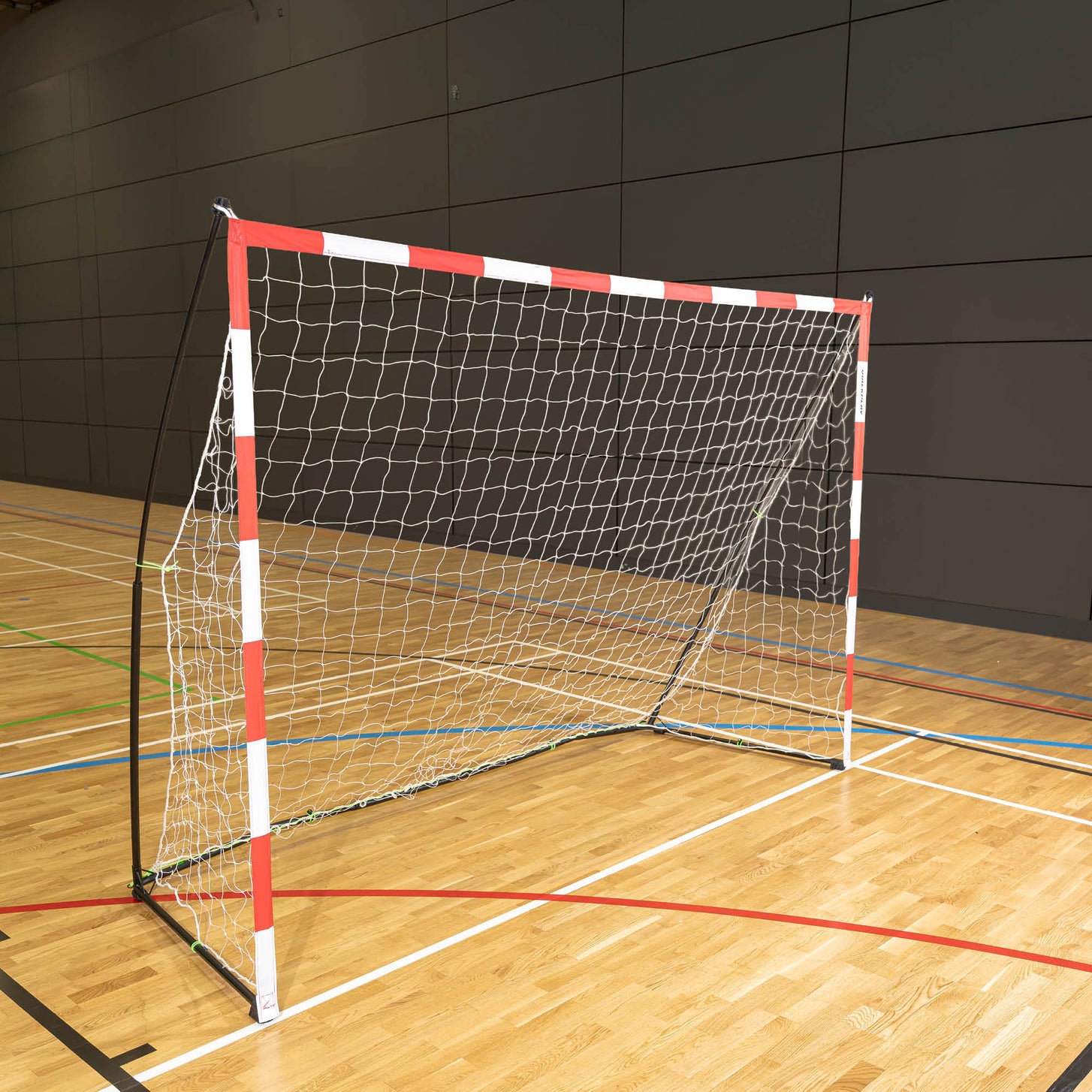 Portable Youth Handball Goal 7.9x5.6' with a red and white frame set up on the wooden floor of an indoor sports hall.