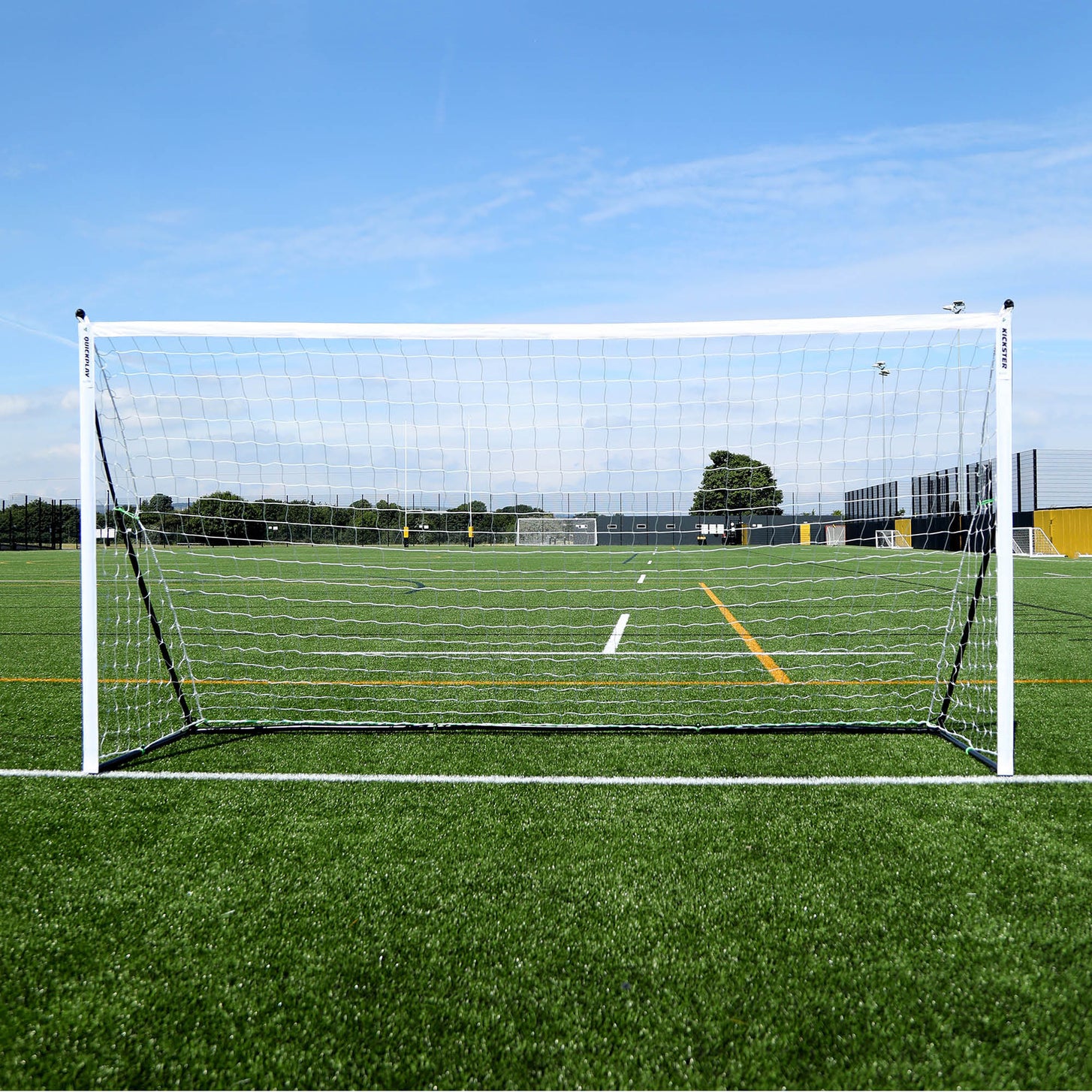 KICKSTER Elite 12x6' goal from the front, white frame and white net on an artificial field under a blue sky.