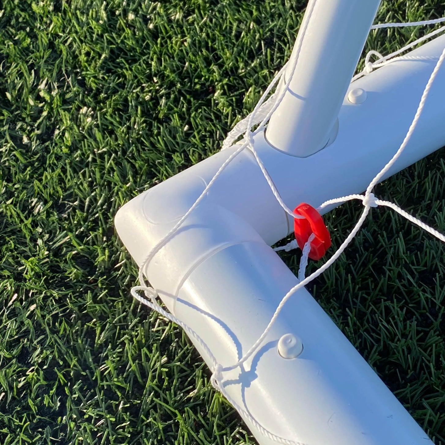 Q-FOLD Folding Soccer Goal 16x7' close-up of a white base corner and red net clip on artificial grass.