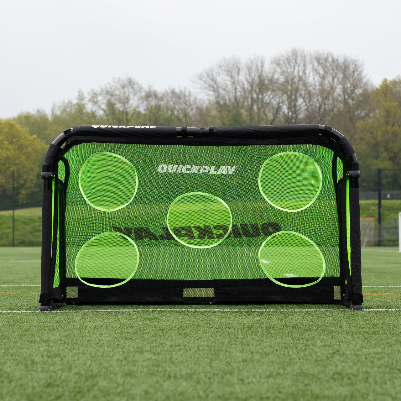 Green QuickPlay Pro Alu soccer goal with a target net on a grass field with trees in the background