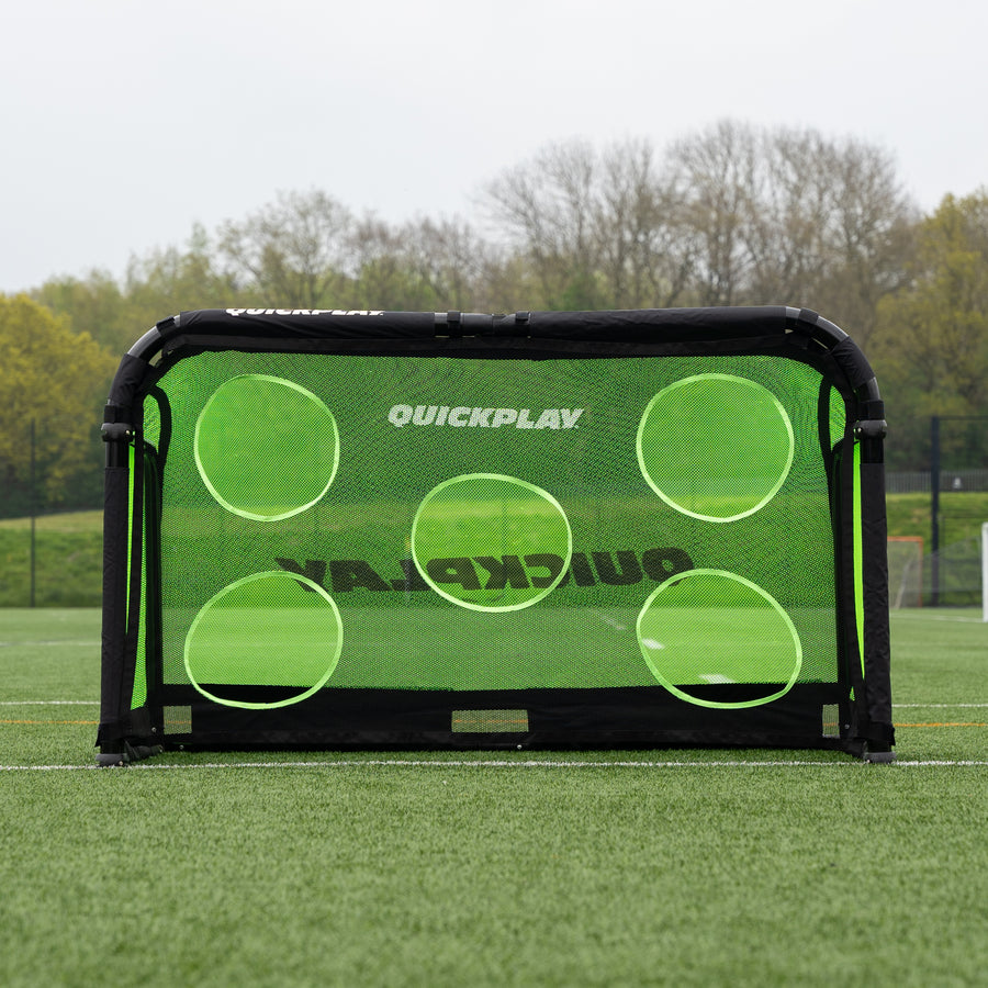 Green QuickPlay Pro Alu soccer goal with a target net on a grass field with trees in the background