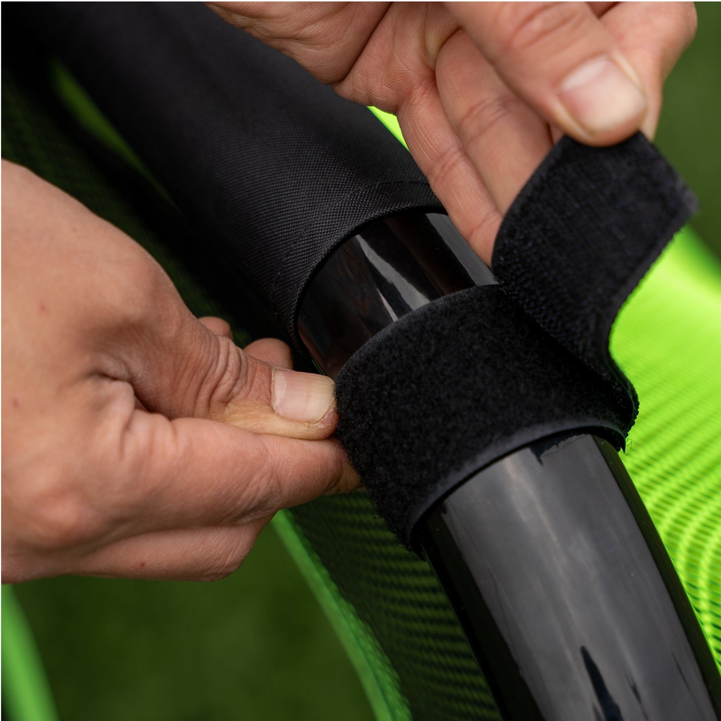PRO ALU Training Target Net Lite 5x3': hands fastening a black hook-and-loop strap around a black goal frame tube.