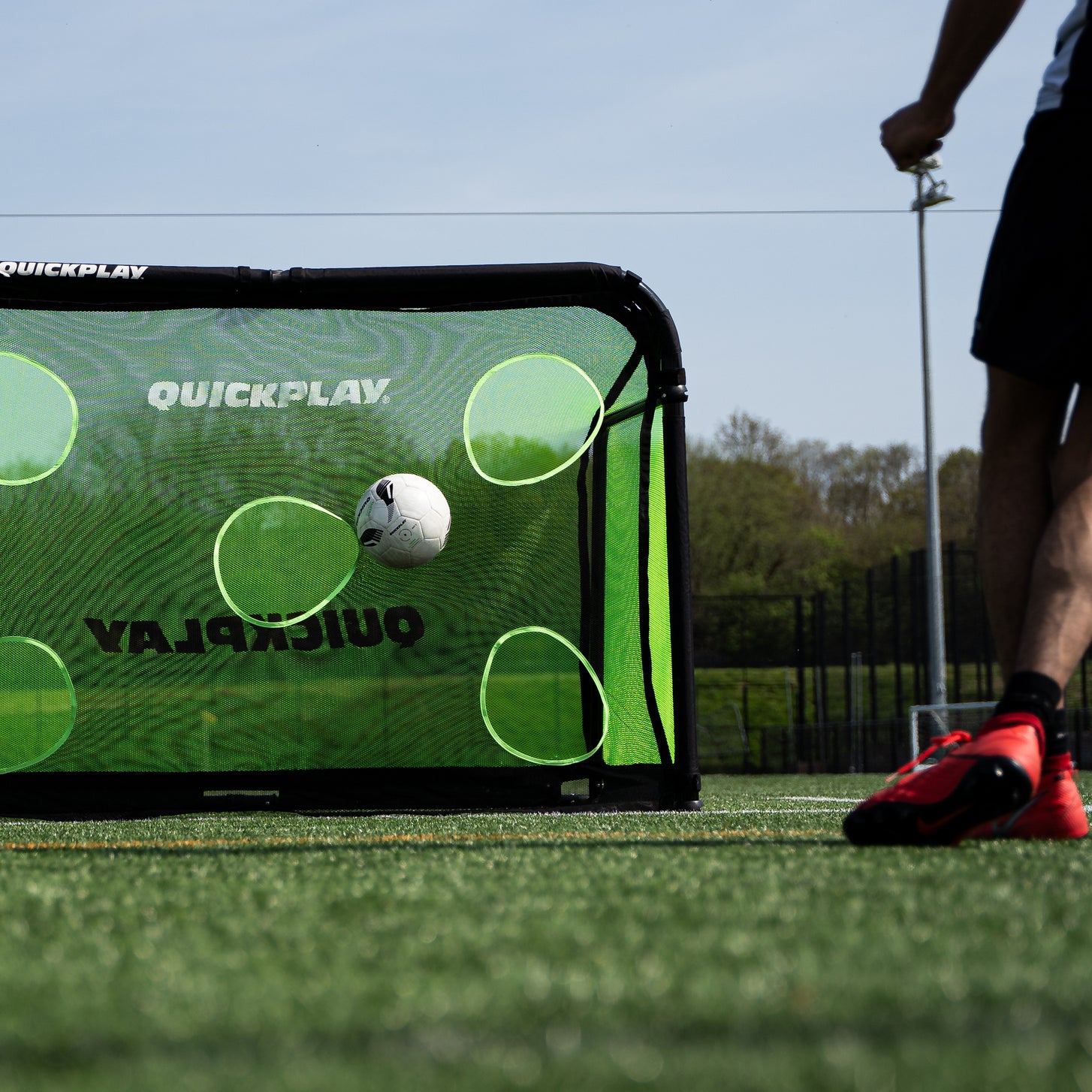 PRO ALU Training Target Net Lite 5x3': a soccer ball flies toward a target hole as a player in red cleats stands beside the goal.