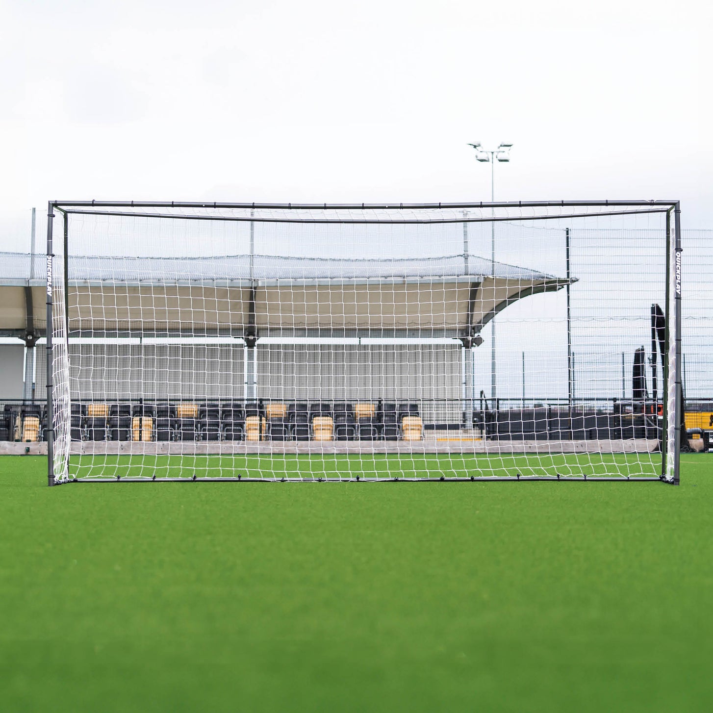GS Series Soccer Goal 16x7' seen from the front on an artificial field, with a covered stadium stand behind.