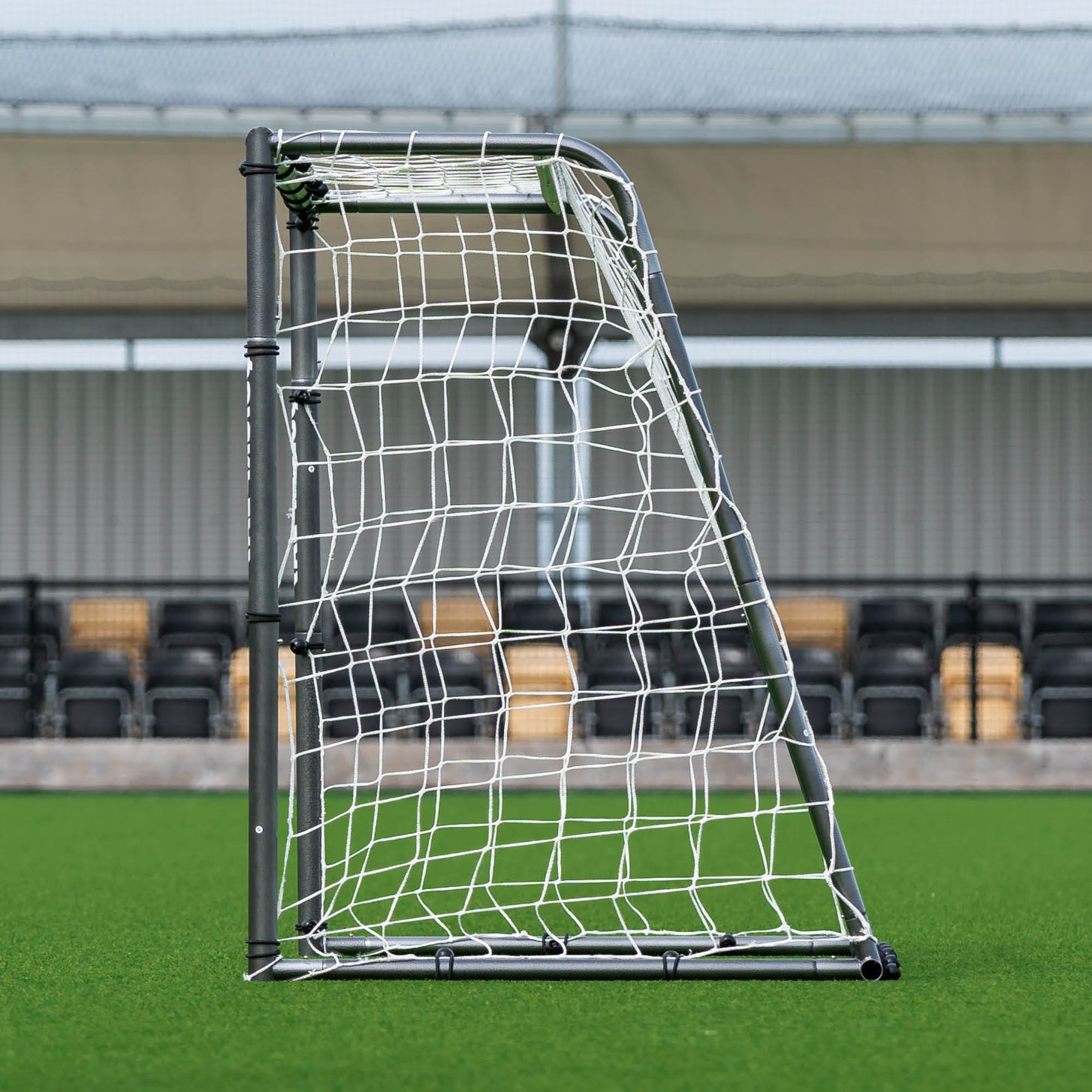 GS Series Soccer Goal 6x4' side view showing its sloped back frame and net, with stadium seats behind.
