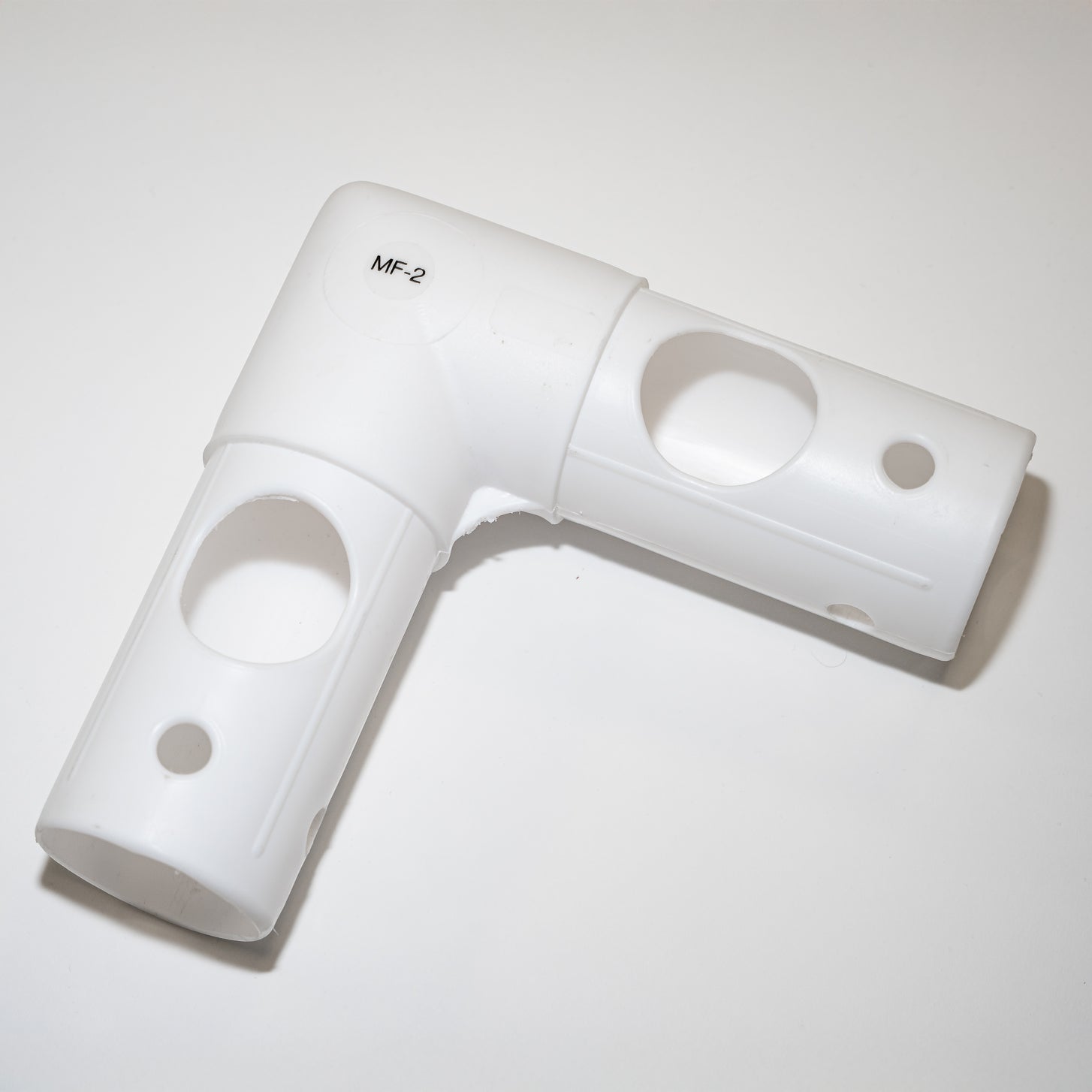 Q-FOLD MF2 tube: a white plastic L-shaped corner connector marked MF-2, with holes in each arm, on a white background.
