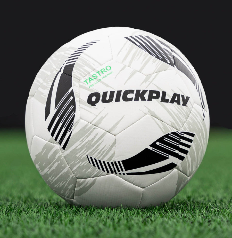 White TASTRO soccer ball with black patterns on a grass field, featuring the brand 'Quickplay'.