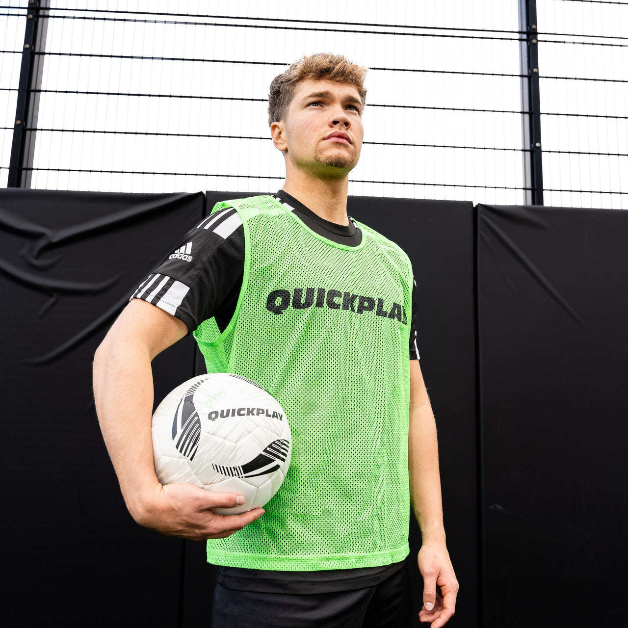 Man holding a soccer ball wearing a green 'Quickplay' pinnie with black text.