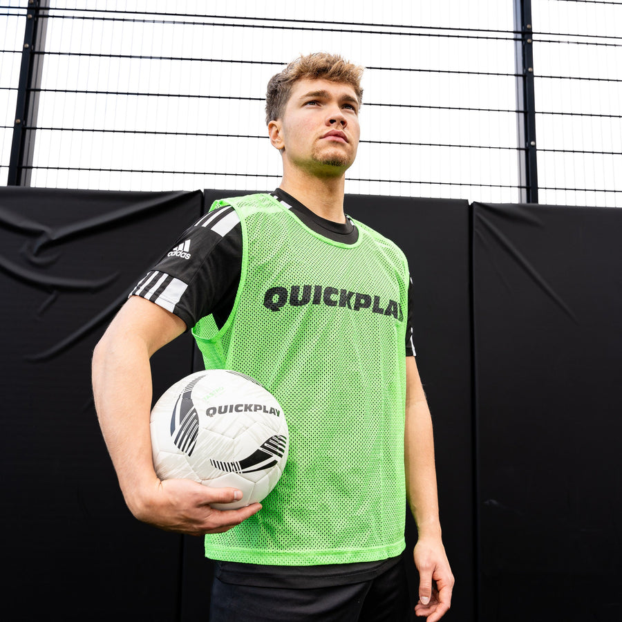 Man holding a soccer ball wearing a green 'Quickplay' pinnie with black text.