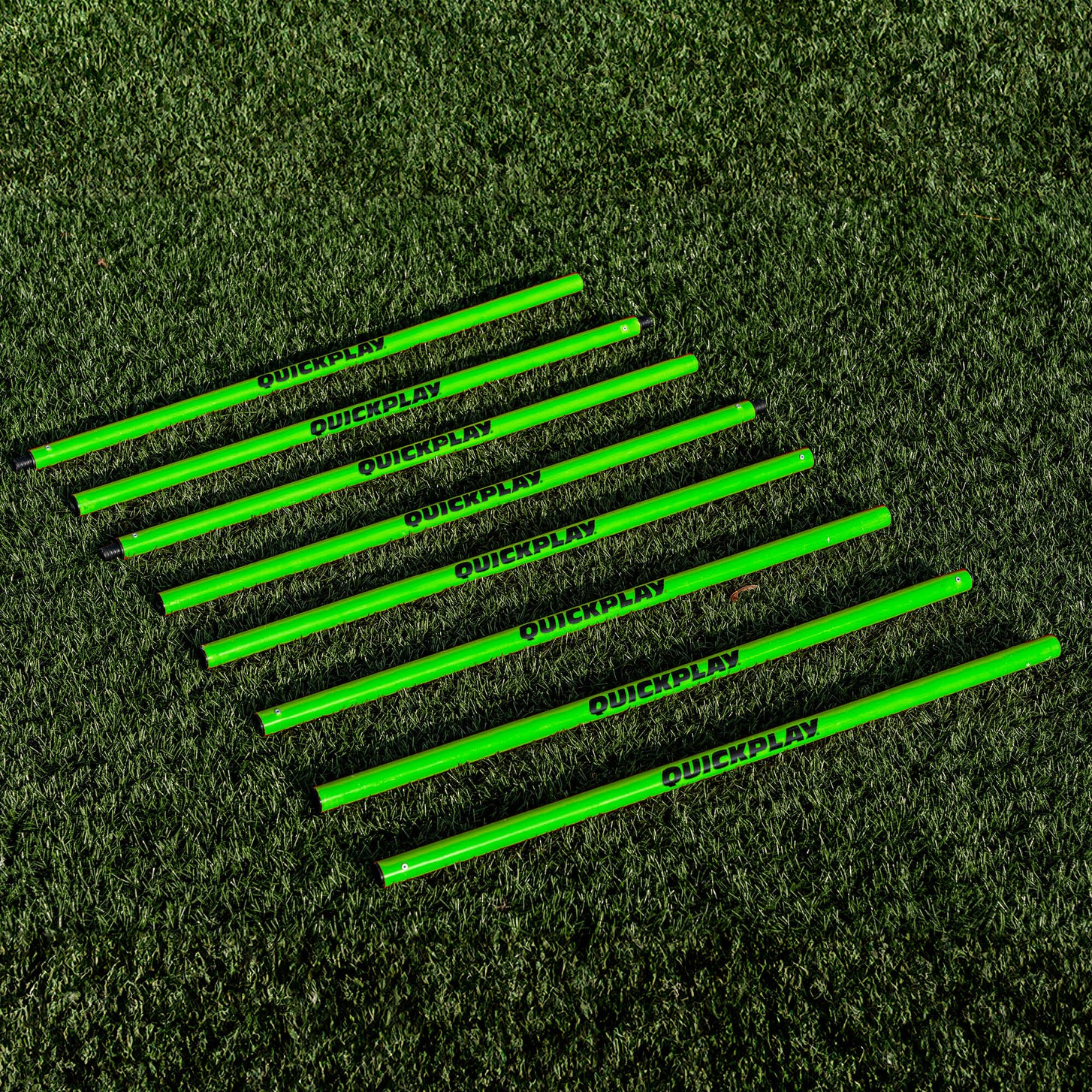 Training Poles: green QUICKPLAY pole sections laid side by side in a row on artificial turf.