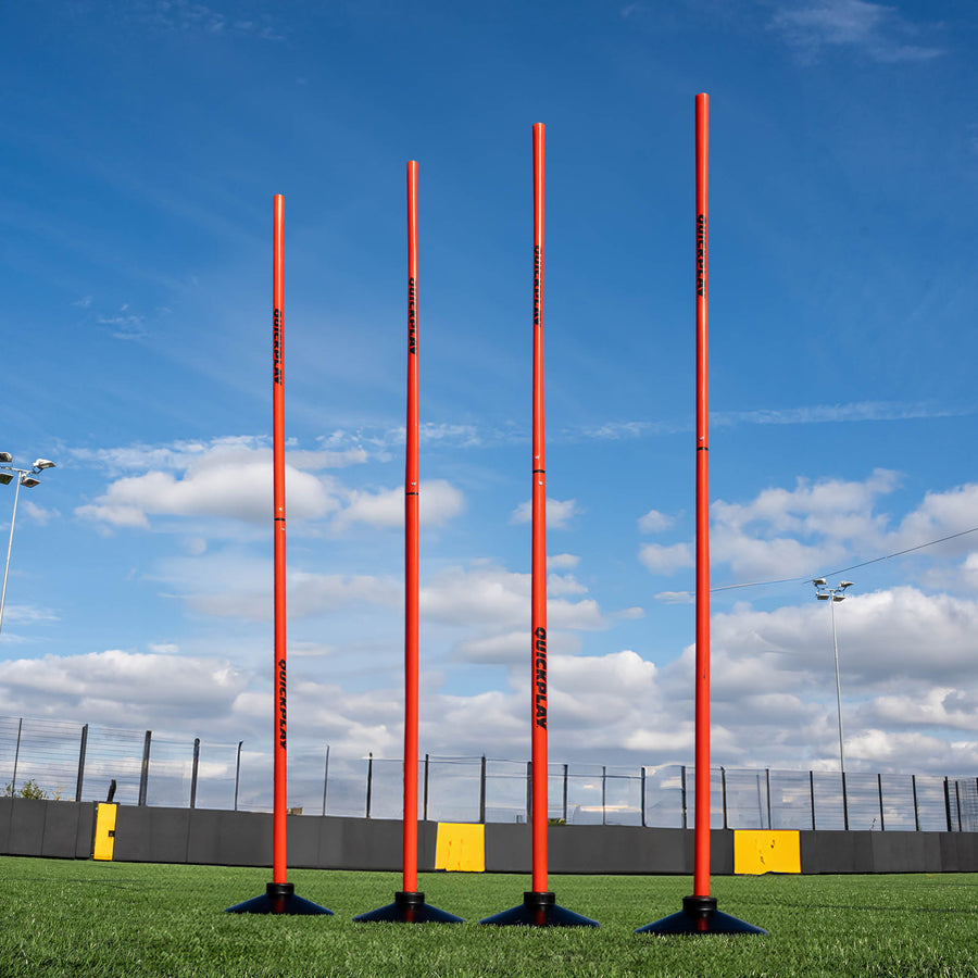 A set of four red training poles with weighted bases on a grass field, designed for speed and agility training.